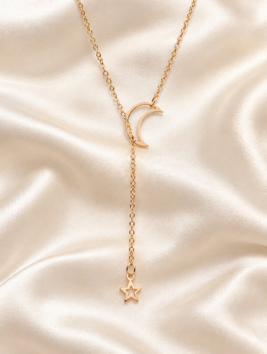 Gold moon and star drop necklace lying on cream silk