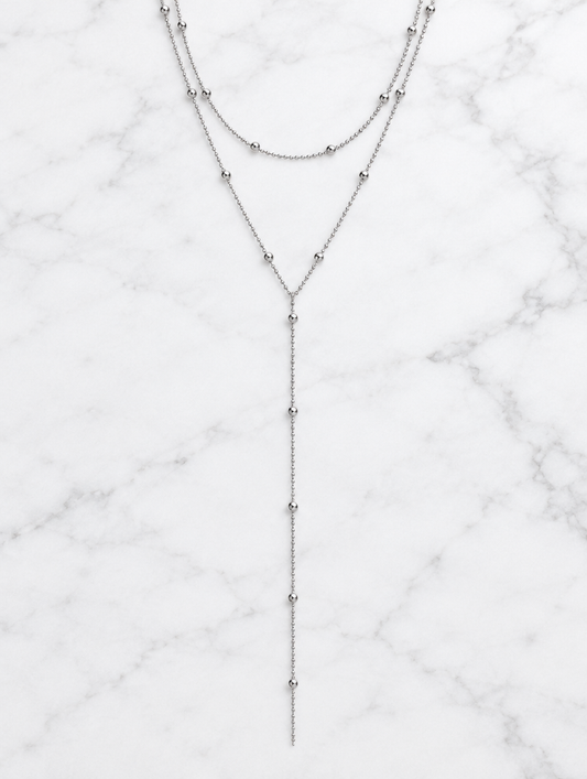 Silver layered lariat necklace lying on white marble