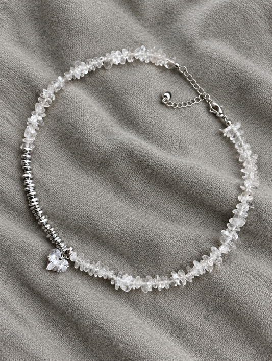 Clear bead choker necklace with heart charm lying on soft grey knit