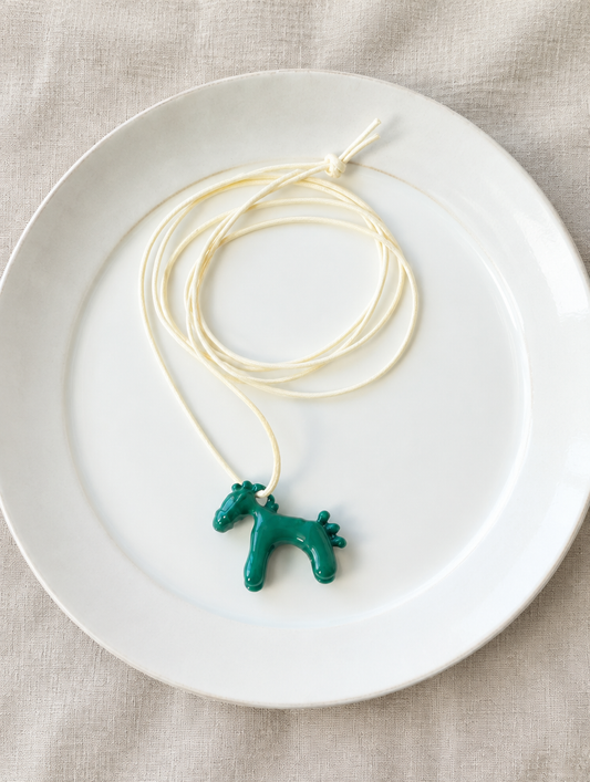 Green horse pendant cord necklace on a white ceramic plate