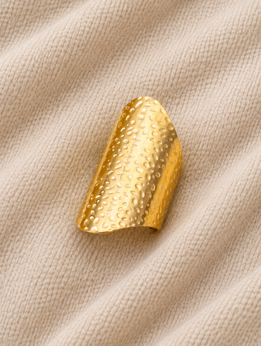Wide gold hammered shield ring resting on a soft textured surface