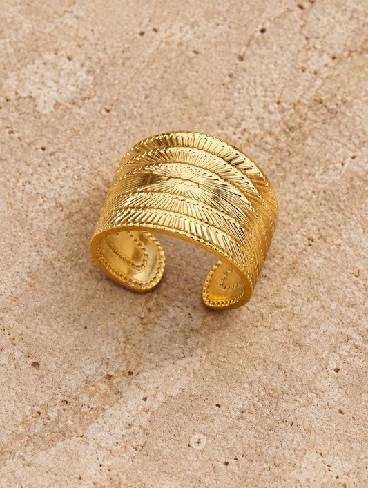 Wide gold ribbed open ring resting on a soft textured surface