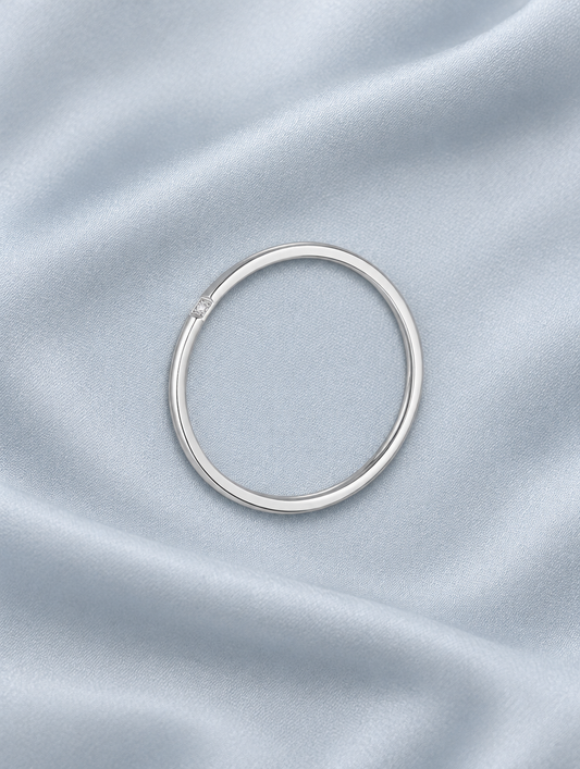 Thin silver stacking ring with a single zirconia resting on a soft textured surface