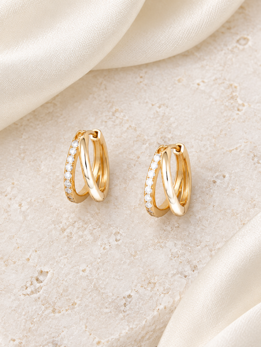 Gold double-ring CZ huggie hoop earrings lying flat on a soft styled surface