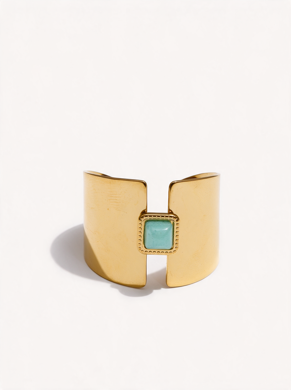Wide gold open ring with square aqua-green stone on a neutral background