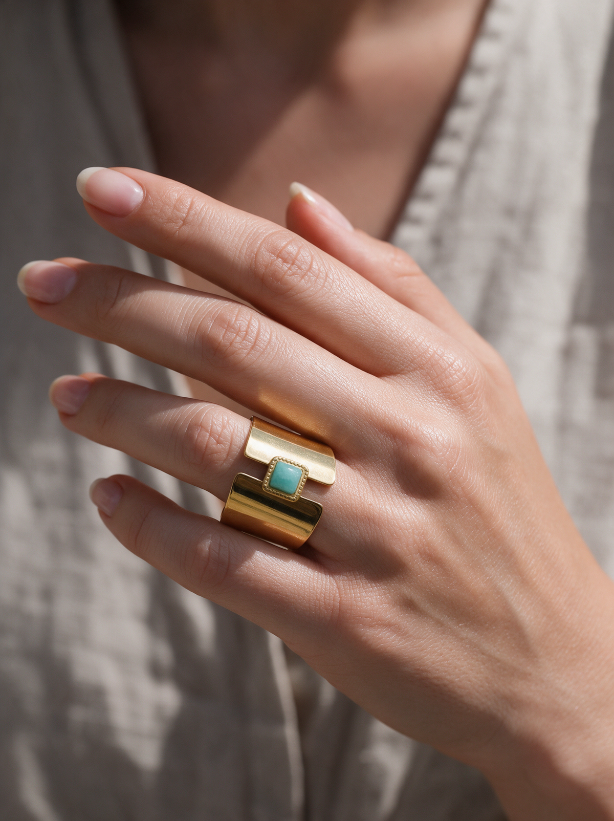 Woman wearing a wide gold open ring with aqua stone on her ring finger