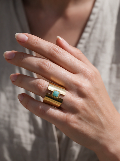 Woman wearing a wide gold open ring with aqua stone on her ring finger