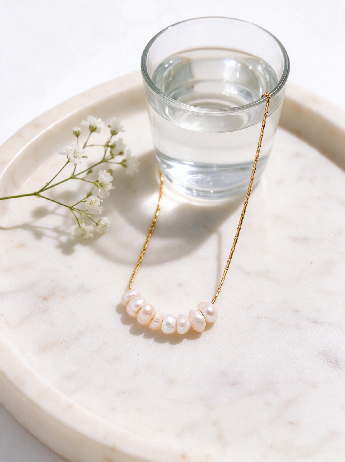 Pearl necklace on a marble tray beside white flowers