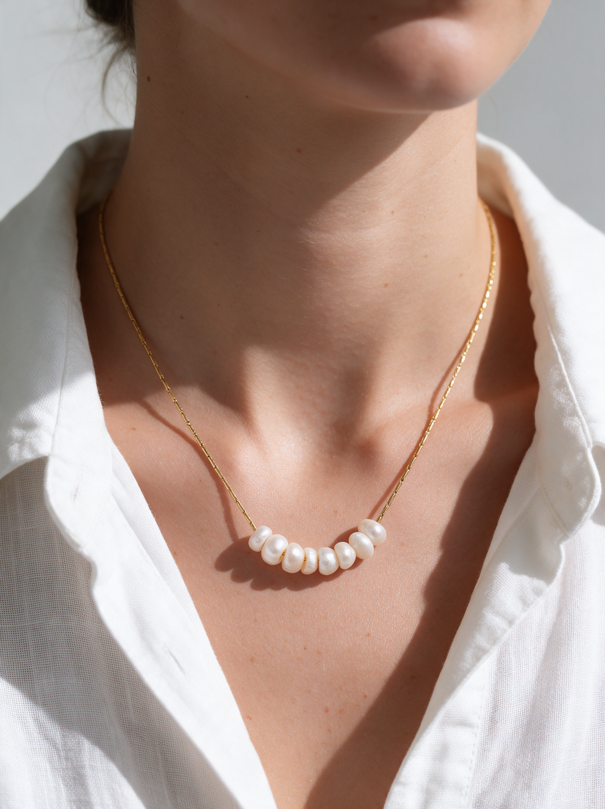 Woman wearing a dainty pearl necklace on a fine gold-tone chain