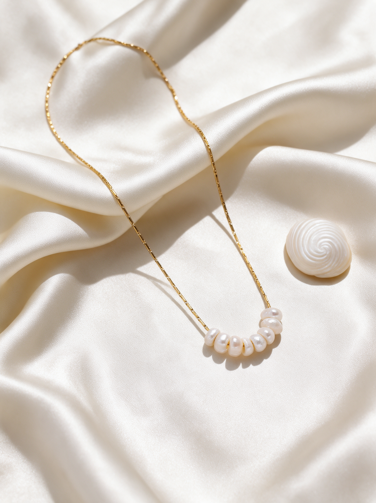 Gold chain pearl necklace draped over cream silk