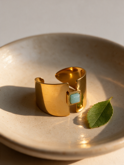 Gold ring with aqua stone on a sand-coloured ceramic dish beside a green leaf