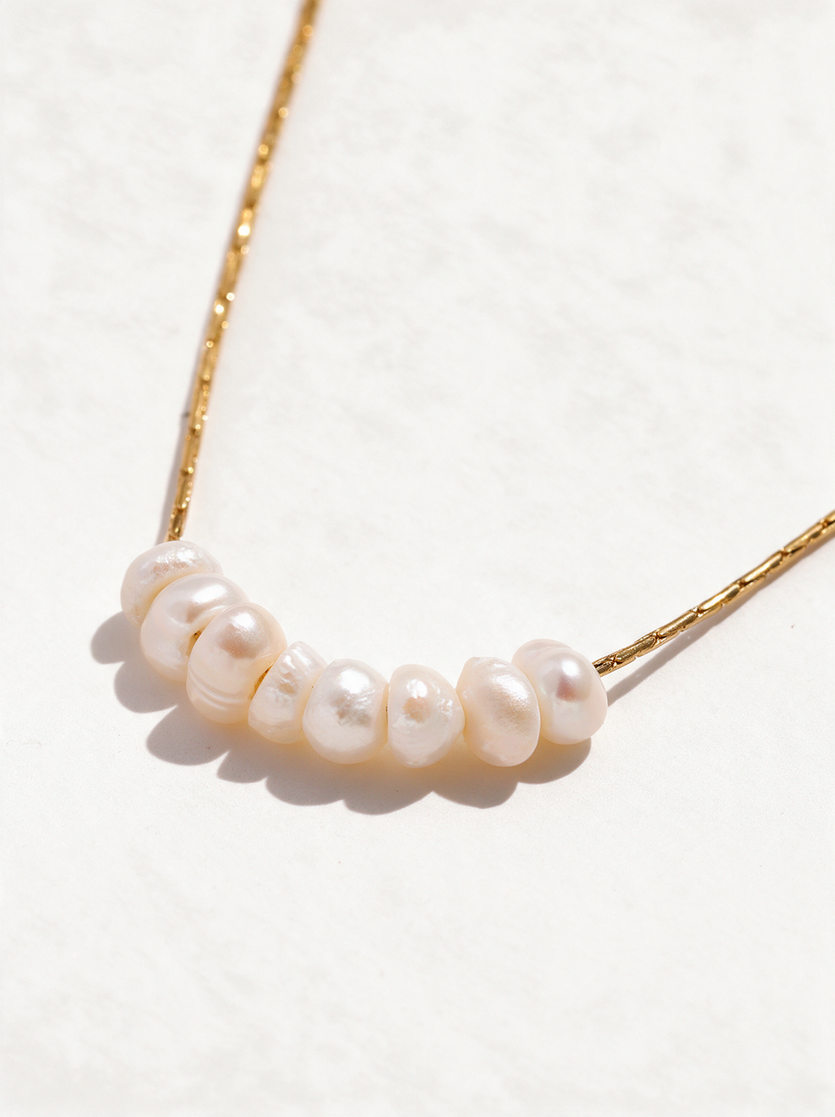 Dainty pearl bead necklace on a fine gold-tone chain on a neutral background