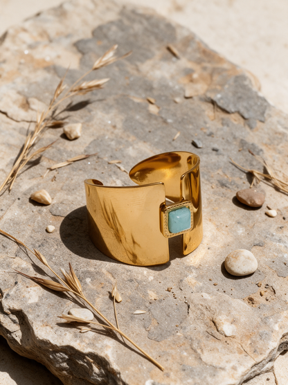 Gold open ring with aqua stone resting on a stone surface with dried grasses