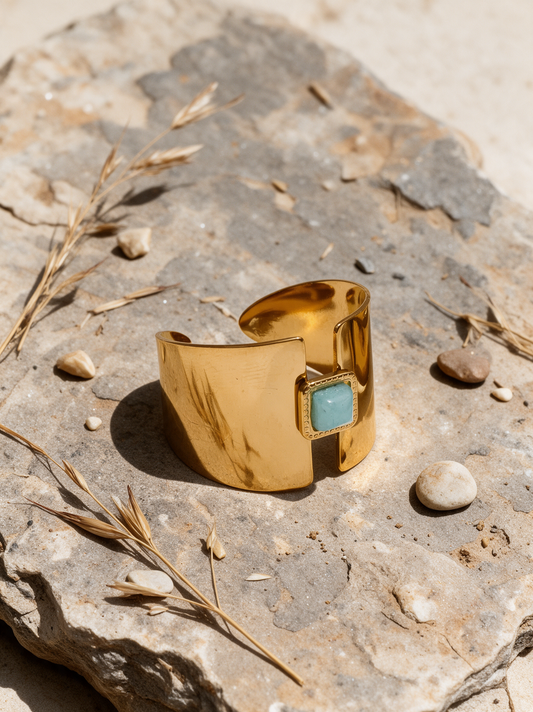 Gold open ring with aqua stone resting on a stone surface with dried grasses