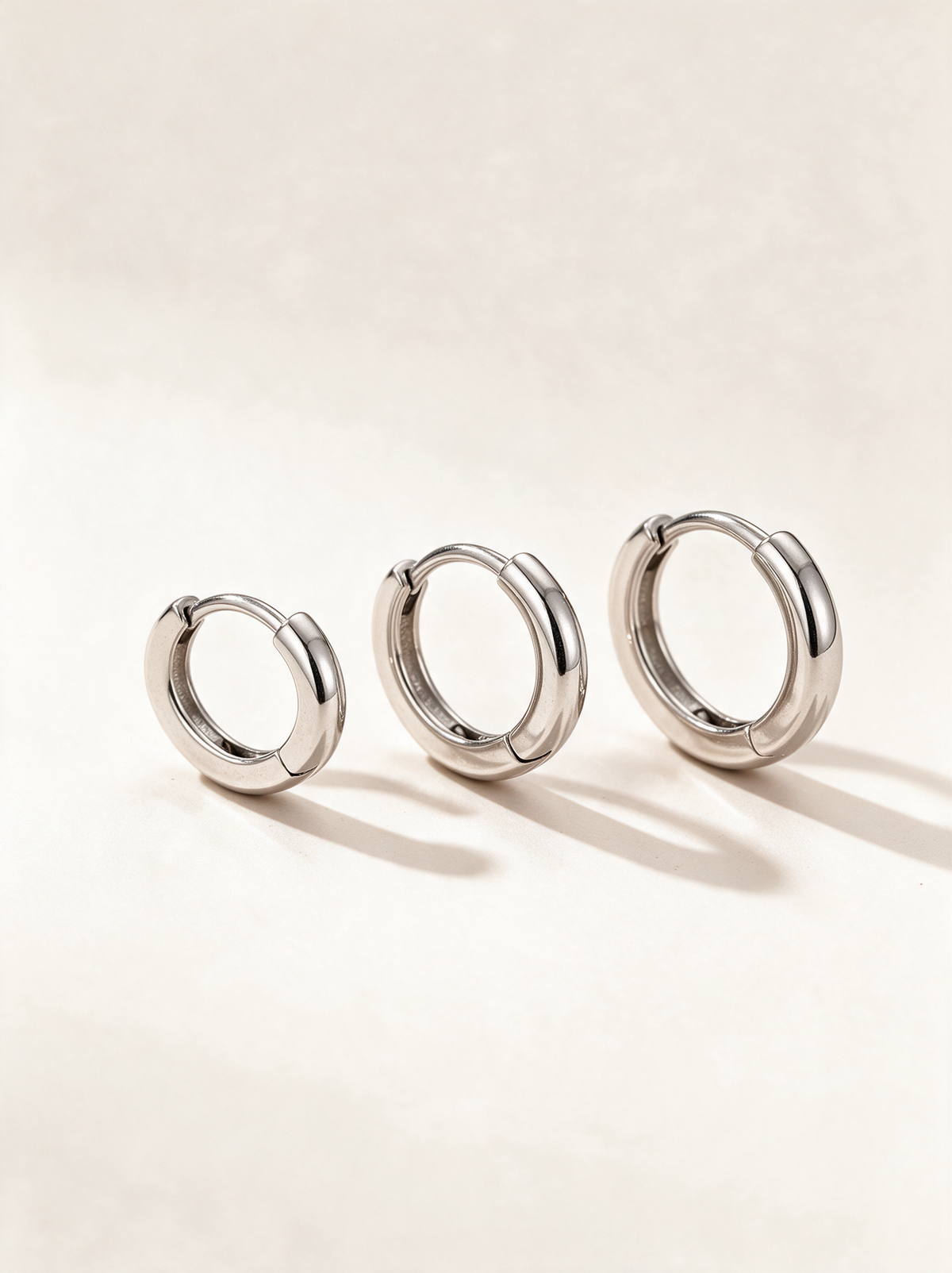 Set of three pairs of silver-tone huggie hoop earrings on a neutral background
