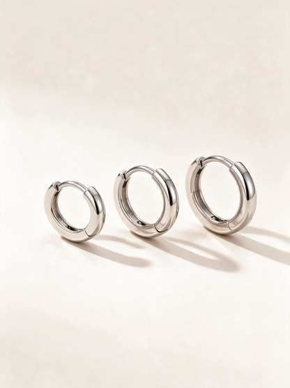 Set of three pairs of silver-tone huggie hoop earrings on a neutral background