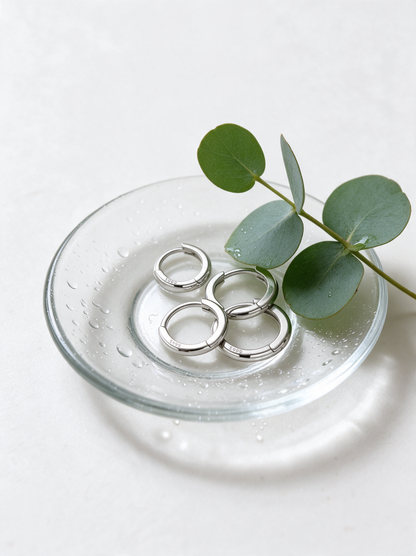 Silver-tone huggie hoops in a glass dish with eucalyptus