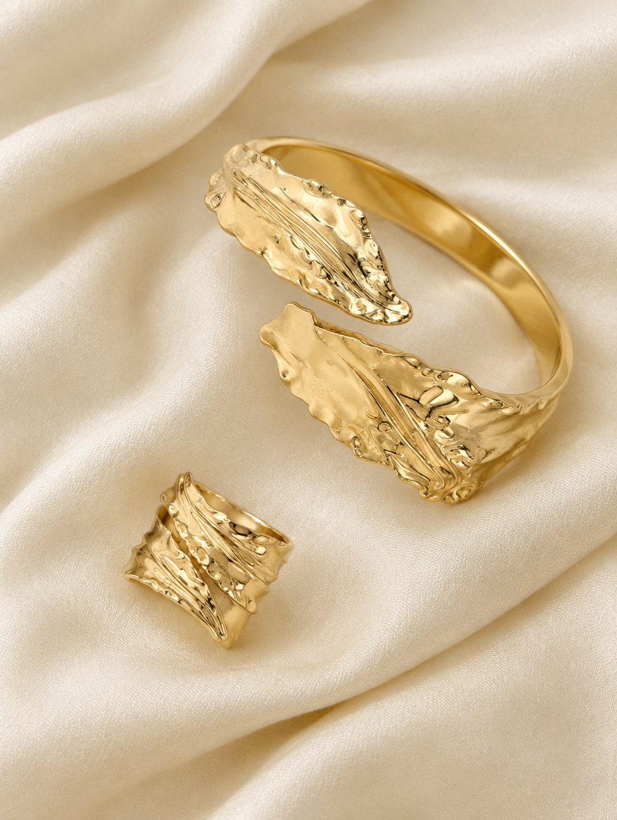 Gold leaf cuff bracelet and ring lying on cream silk