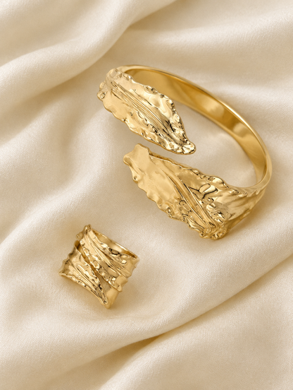 Gold leaf cuff bracelet and ring lying on cream silk