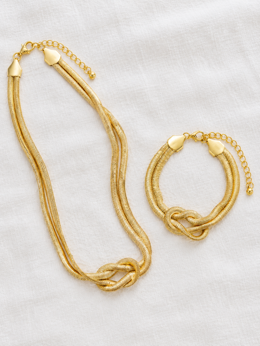 Gold knot necklace and bracelet set lying on white linen