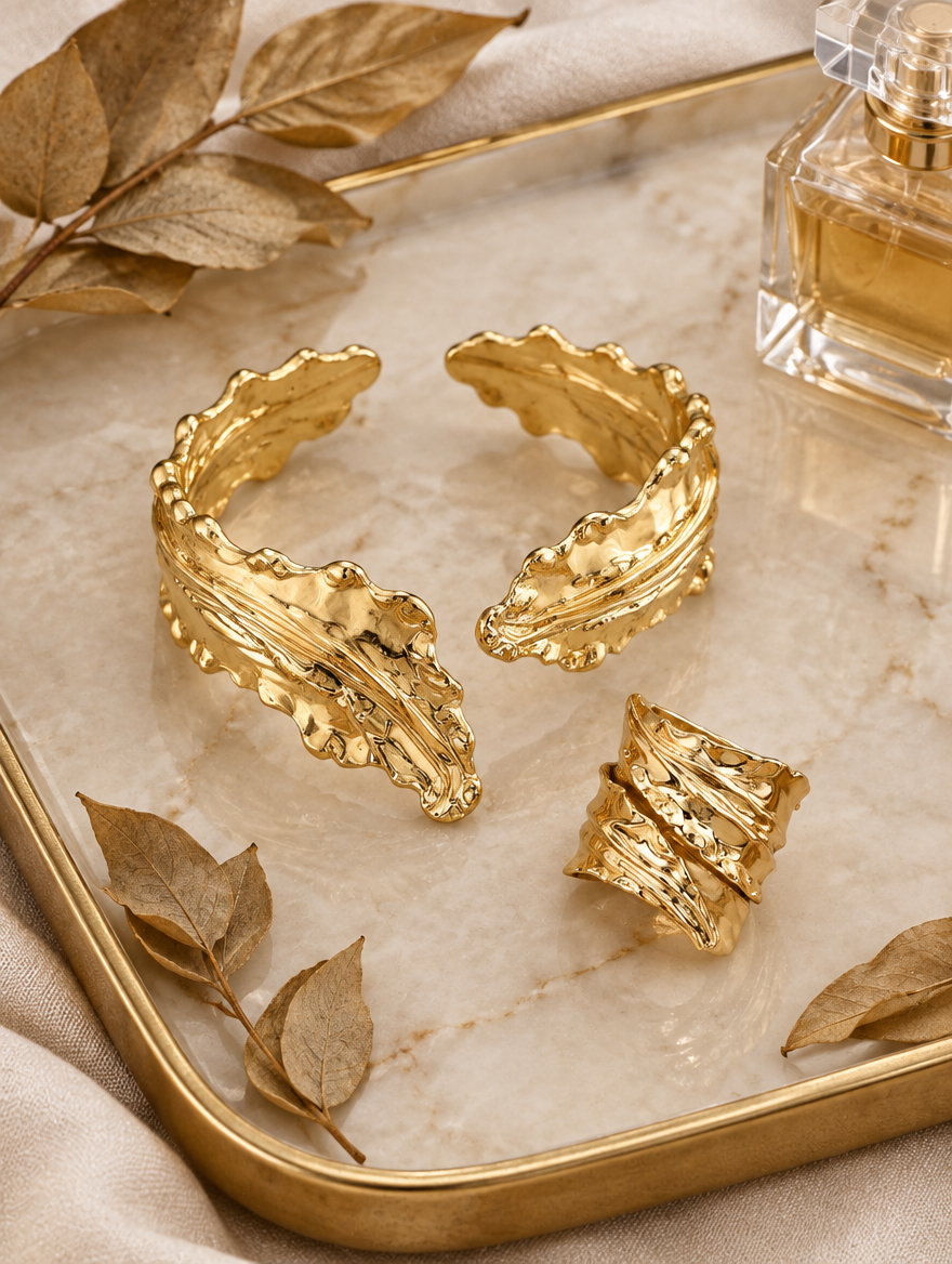 Gold leaf cuff bracelet and ring on a marble tray with dried leaves