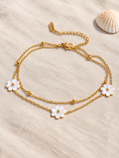 Gold flower charm anklet on sand-coloured linen with a seashell