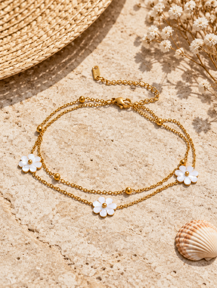 Gold anklet with white flowers beside a straw hat and a seashell