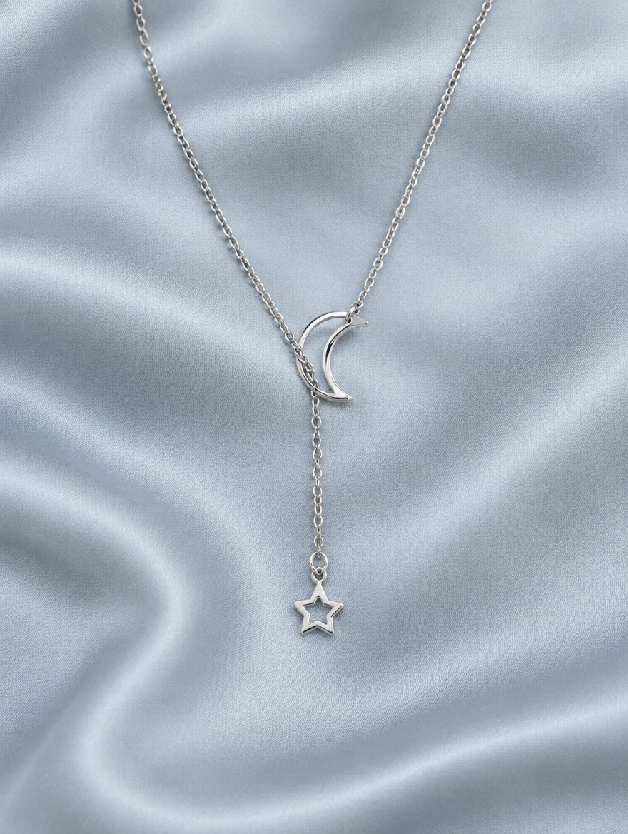 Silver moon and star drop necklace lying on blue-grey silk