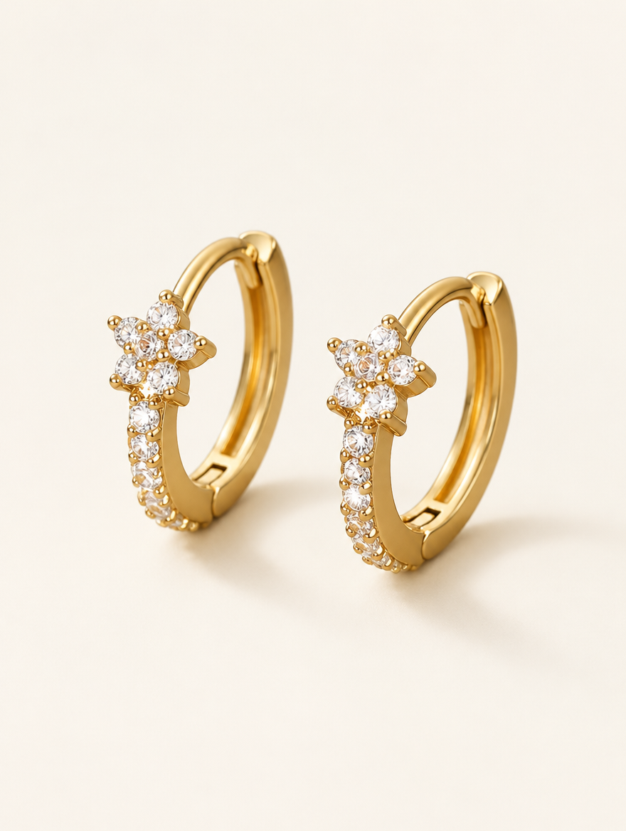Pair of gold huggie hoop earrings with cz flower cluster on a warm off-white background