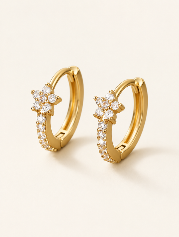 Pair of gold huggie hoop earrings with cz flower cluster on a warm off-white background