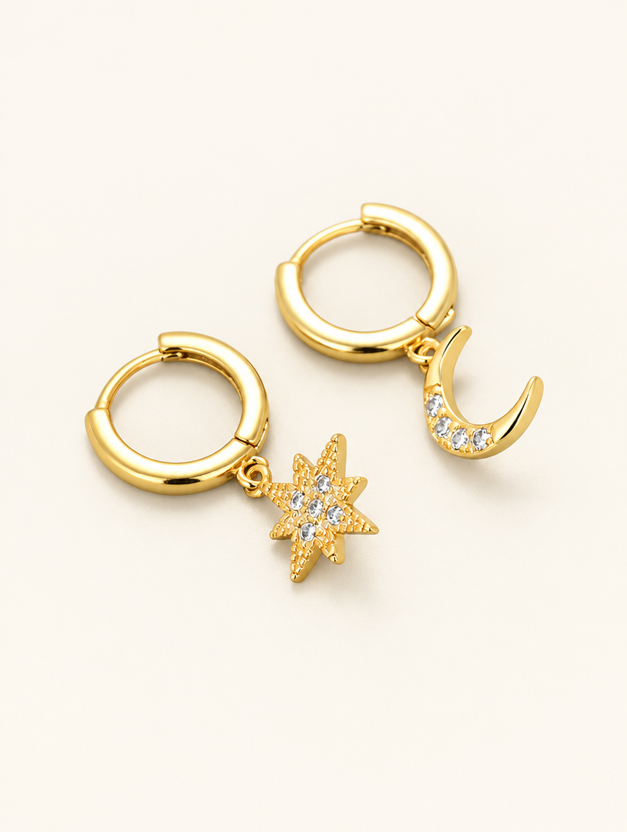 Pair of gold star and moon cz huggie hoop earrings on a warm off-white background