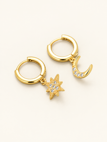 Pair of gold star and moon cz huggie hoop earrings on a warm off-white background