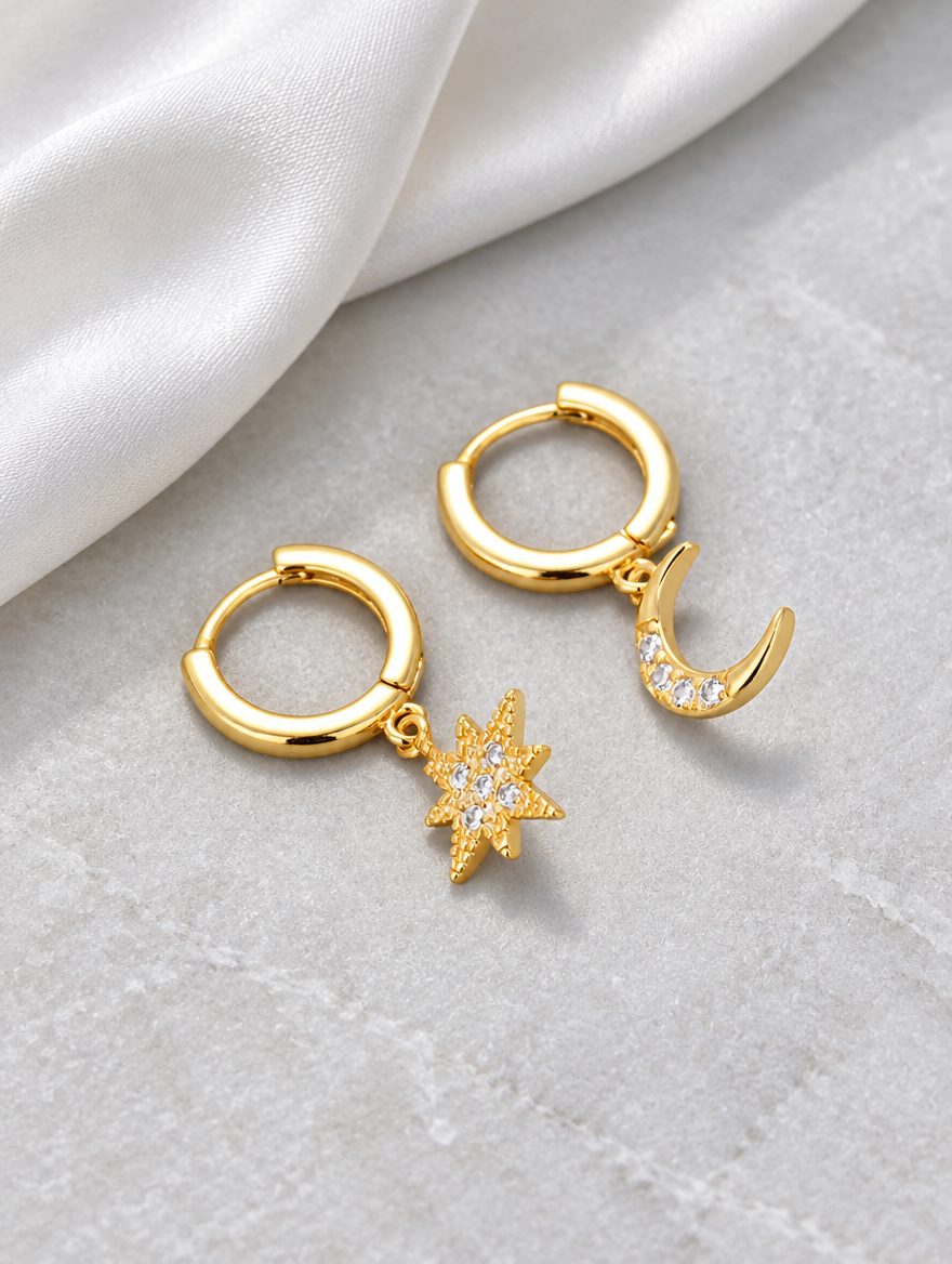 Gold star and moon cz huggie hoop earrings lying flat on a soft styled surface