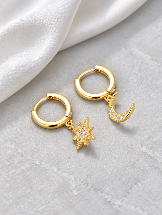Gold star and moon cz huggie hoop earrings lying flat on a soft styled surface
