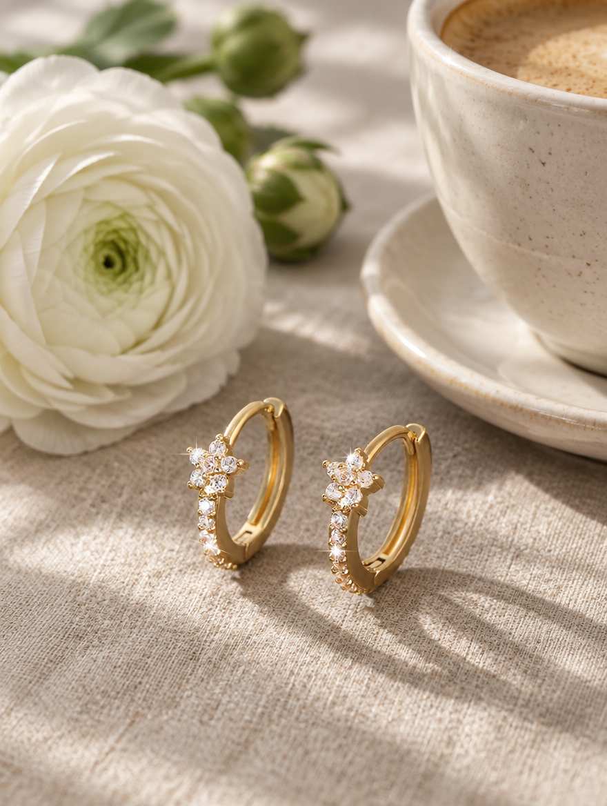 Gold huggie hoop earrings with cz flower cluster in a styled still life with props