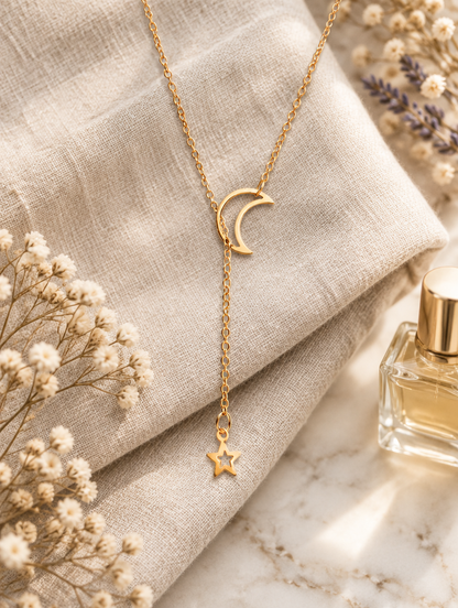 Gold lariat necklace with moon and star beside dried flowers and perfume