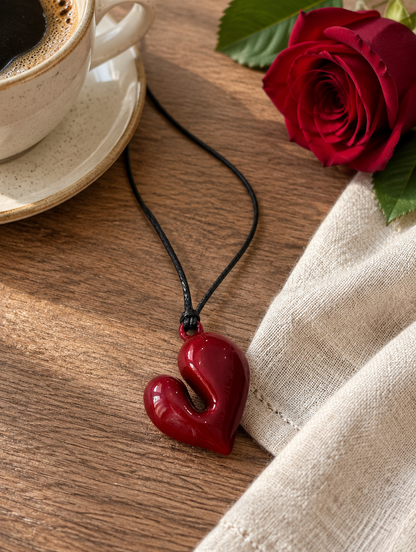 Red heart cord necklace beside a coffee cup and a red rose on a wooden table