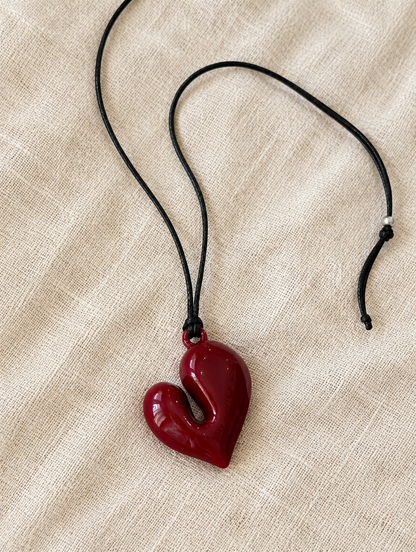 Red heart pendant cord necklace lying on beige linen