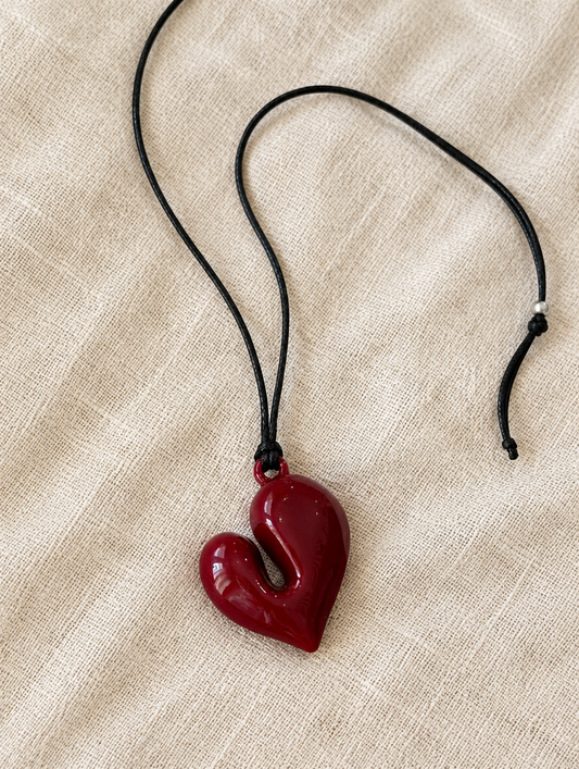 Red heart pendant cord necklace lying on beige linen