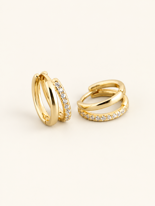 Pair of gold double-band huggie hoop earrings with cz stones on a warm off-white background