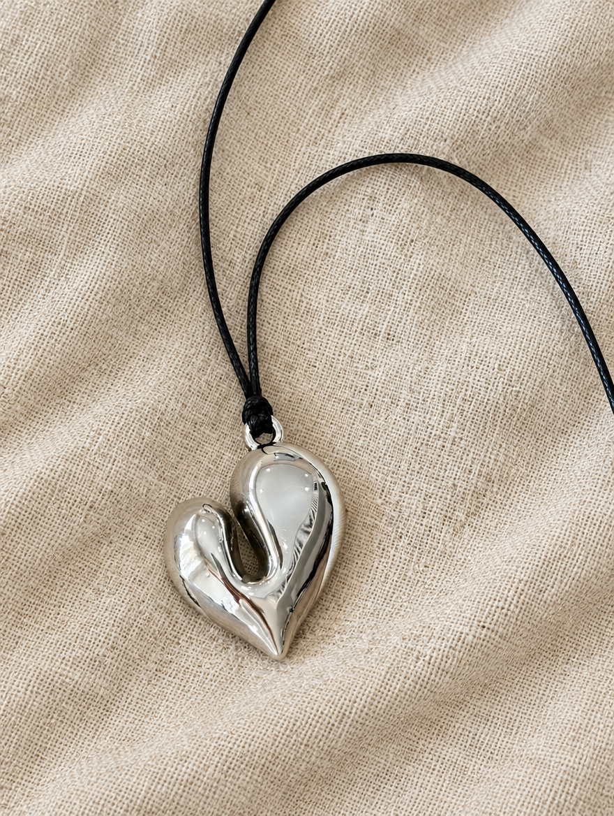 Silver heart pendant cord necklace lying on beige linen