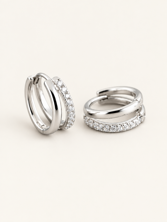 Pair of silver double-band huggie hoop earrings with cz stones on a warm off-white background