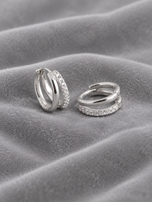 Silver double-band huggie hoop earrings with cz stones lying flat on a soft styled surface