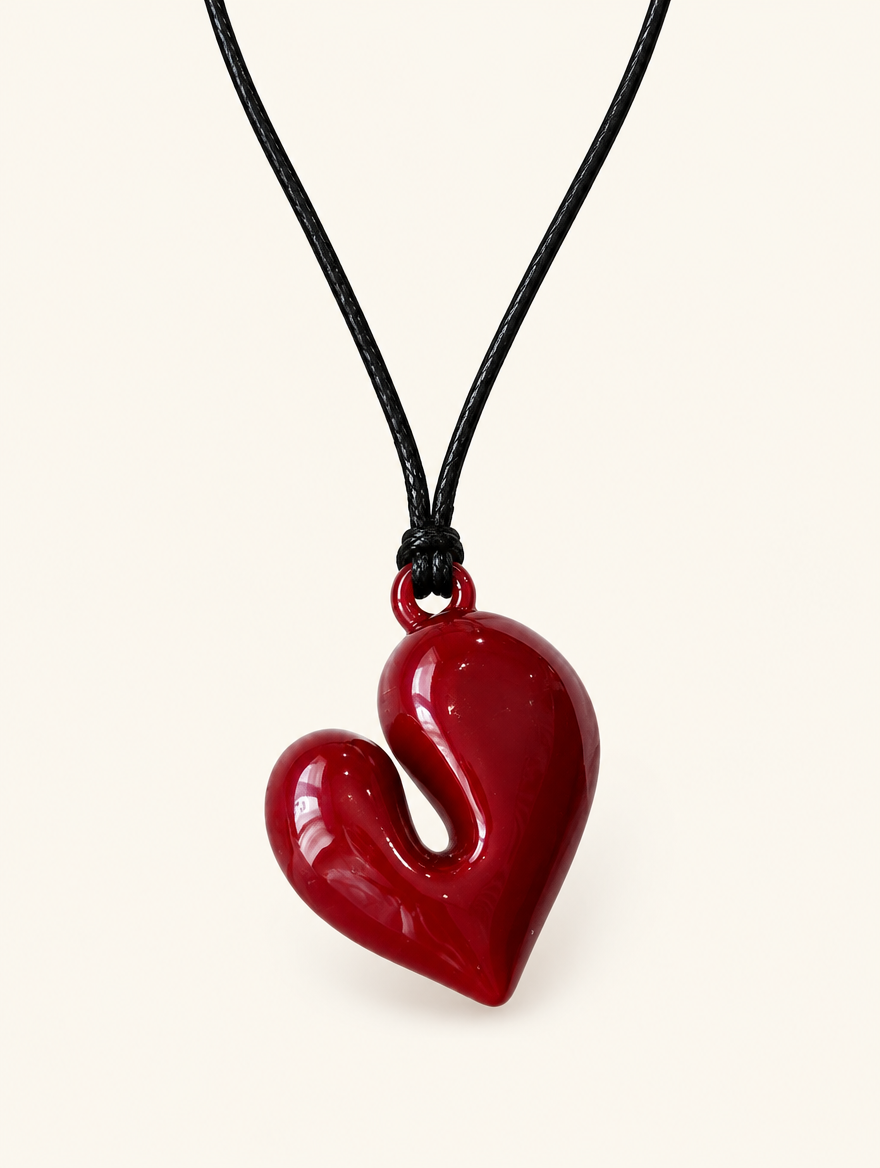 Dark red glossy heart pendant on a black cord necklace on a neutral background