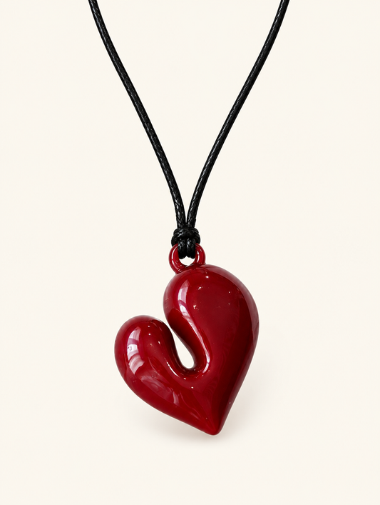 Dark red glossy heart pendant on a black cord necklace on a neutral background