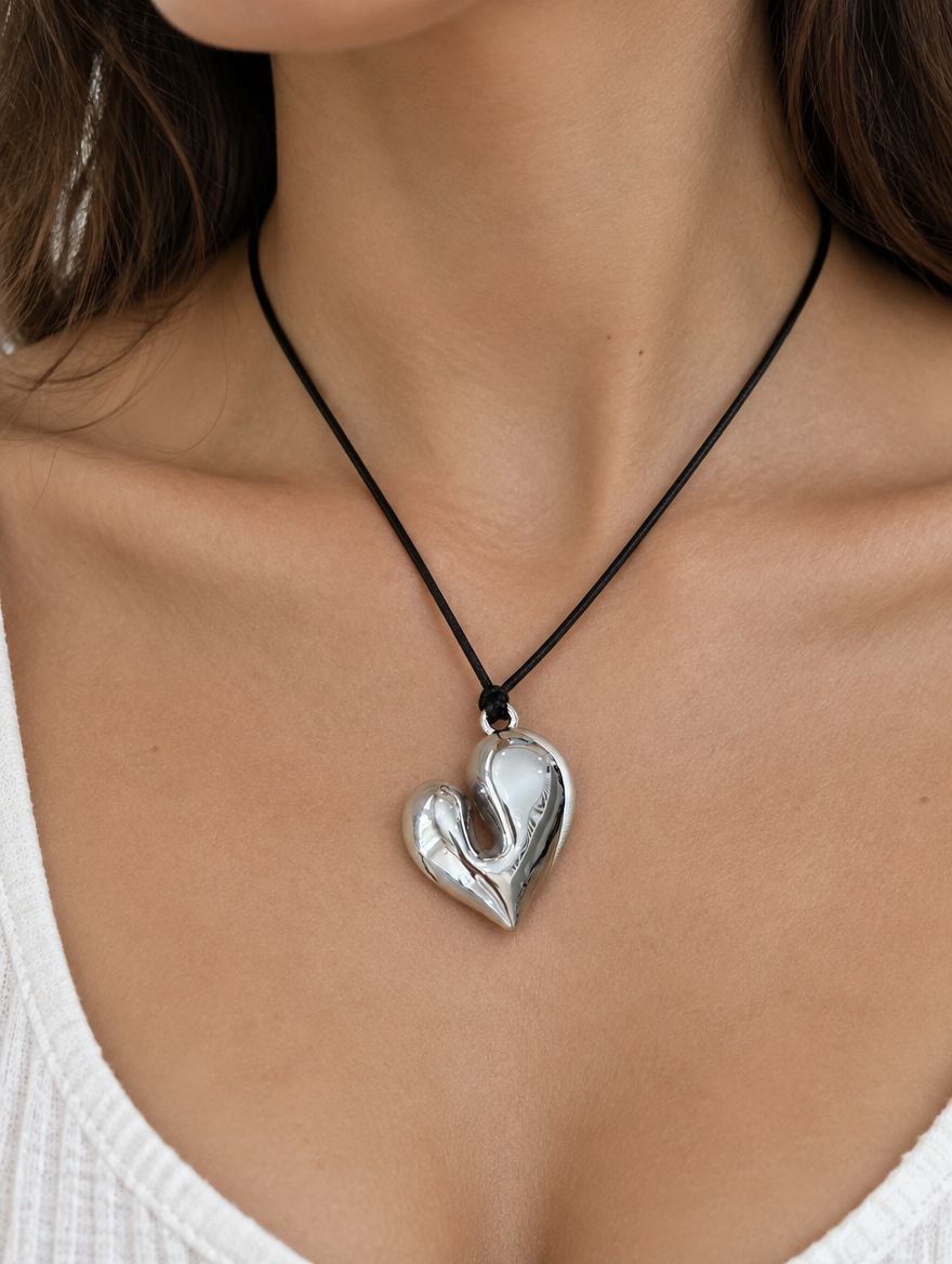 Woman wearing a black cord necklace with a glossy silver heart pendant