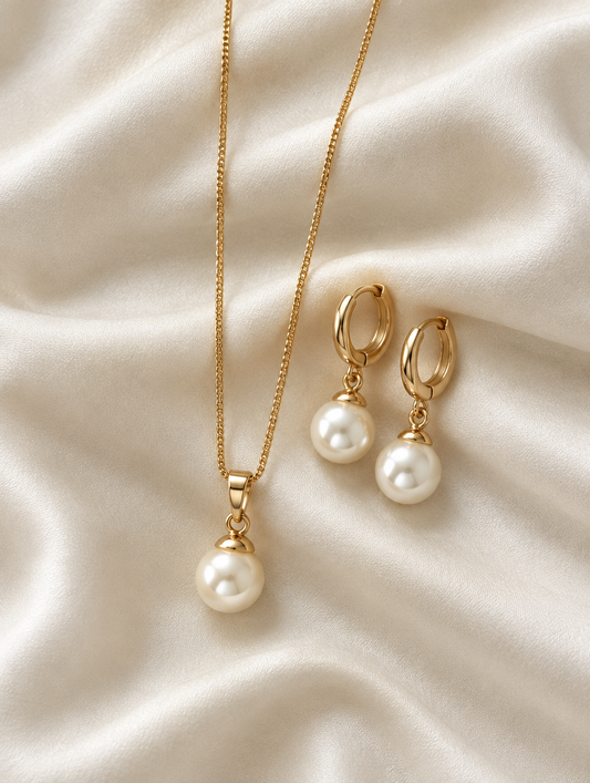 Gold pearl pendant necklace and earrings lying on ivory silk