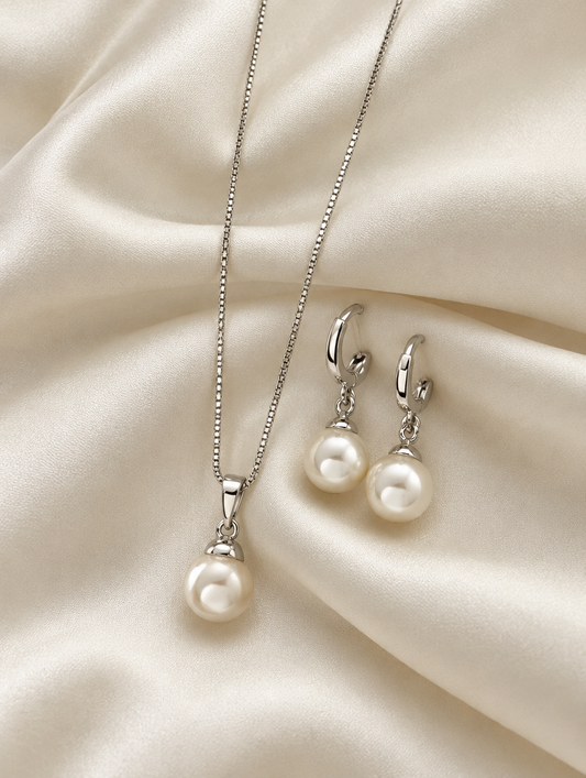 Silver pearl pendant necklace and earrings lying on ivory silk