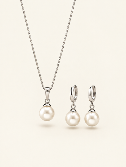 Silver pearl pendant necklace and drop hoop earrings set on a neutral background