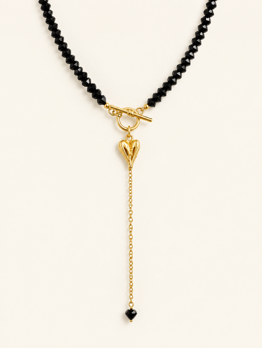 Black bead necklace with a gold-tone toggle clasp and heart charm on a neutral background